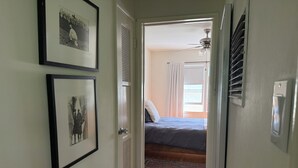 En hall som leder till ett sovrum med en säng, en takfläkt och ett fönster med gardiner.