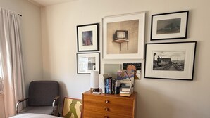 Ett sovrum med en säng, en stol, en byrå med böcker och inramade bilder på väggen.