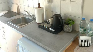 A kitchen with wooden cabinets, a white refrigerator, a coffee maker, a kettle, a sink, and two water bottles. - Kalymnos getaway atop Linaria Beach (Kalimnos)
