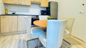 A compact kitchen with wooden cabinets, a stainless steel refrigerator, a coffee maker, and a dining table with white chairs. - Modern 3BR Apartment 10 Min to FAC Platz (Wien)