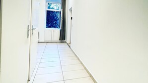 A hallway with white walls and a tiled floor leading to a room with a window. - Modern 3BR Apartment 10 Min to FAC Platz (Wien)