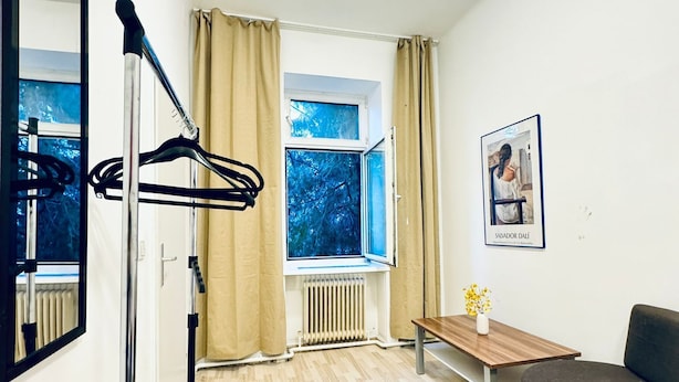 A modern room with a wooden floor, a radiator, a window with curtains, a bench, a sofa, and a framed picture on the wall. - Modern 3BR Apartment 10 Min to FAC Platz (Wien)