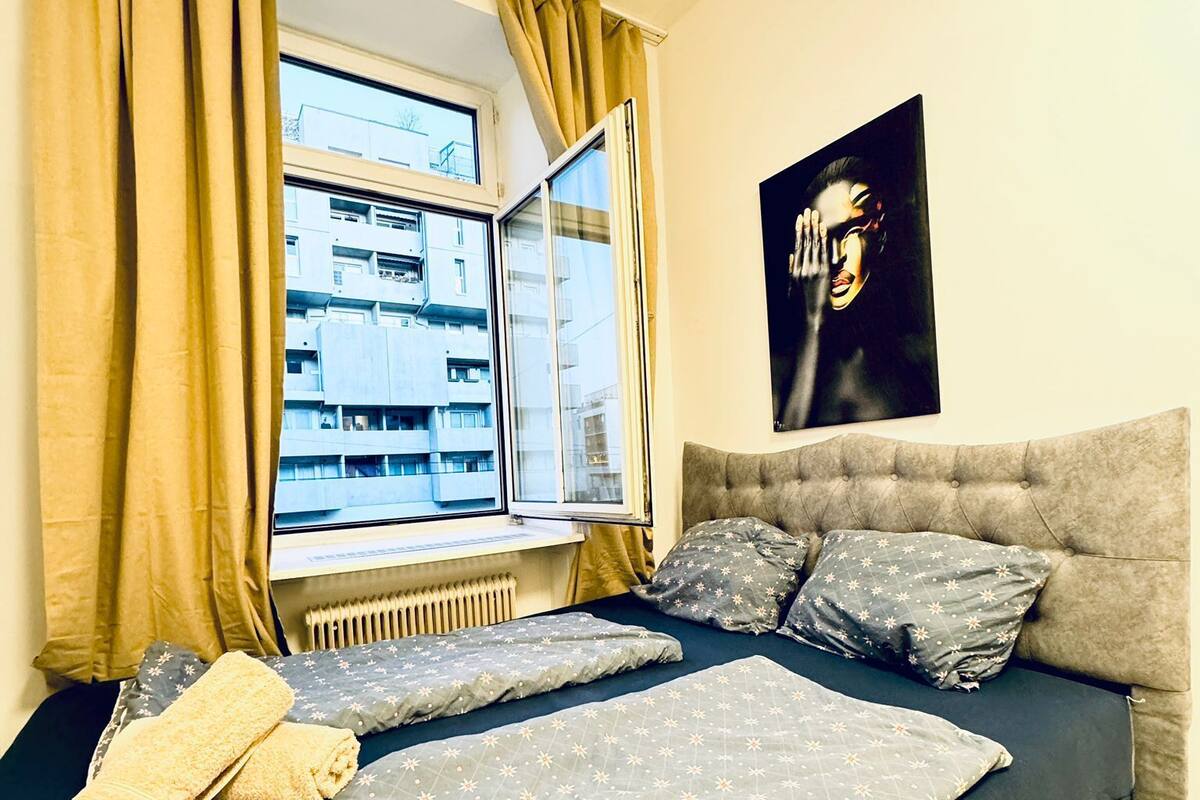 A bedroom with a bed, a window, a radiator, and a painting on the wall.