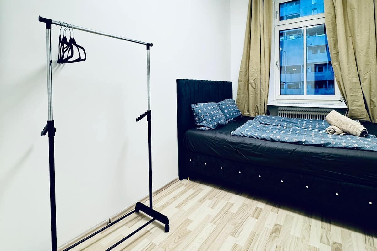 A bedroom with a bed, a wardrobe, a window with curtains, and a light fixture.