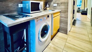 A compact kitchen with wooden cabinets, a microwave, a washing machine, and a sink. - Modern Studio for 3 Near FAC Platz (Wien)