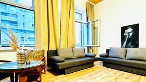 A living room with a wooden floor, two sofas, a round table, and a window with curtains. - Modern Studio for 3 Near FAC Platz (Wien)