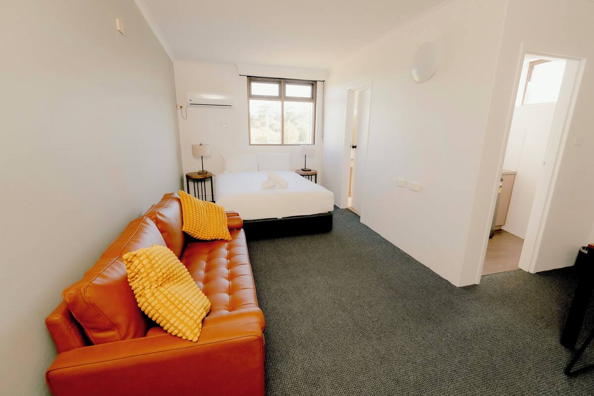 Une chambre à coucher comprenant un lit, un canapé, une fenêtre et une porte donnant sur une autre pièce.