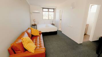 A bedroom with a bed, a sofa, a window, and a door leading to another room.