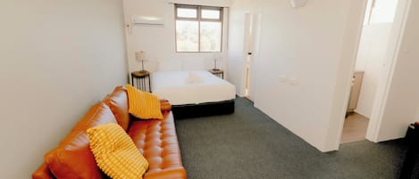 A bedroom with a bed, a sofa, a window, and a door leading to another room.
