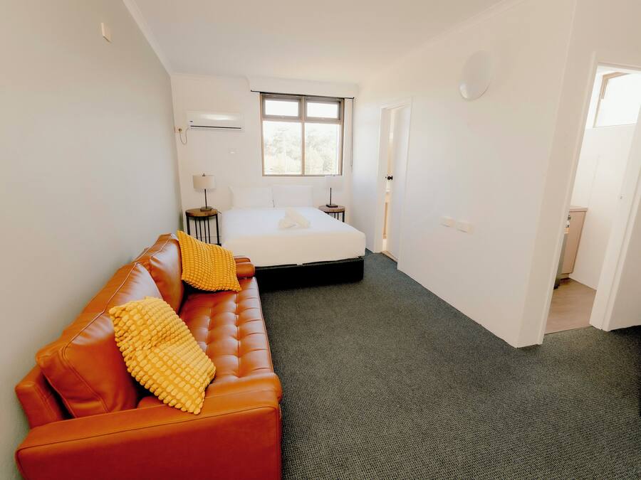 Un dormitorio con cama, sofá, ventana y puerta que da a otra habitación.