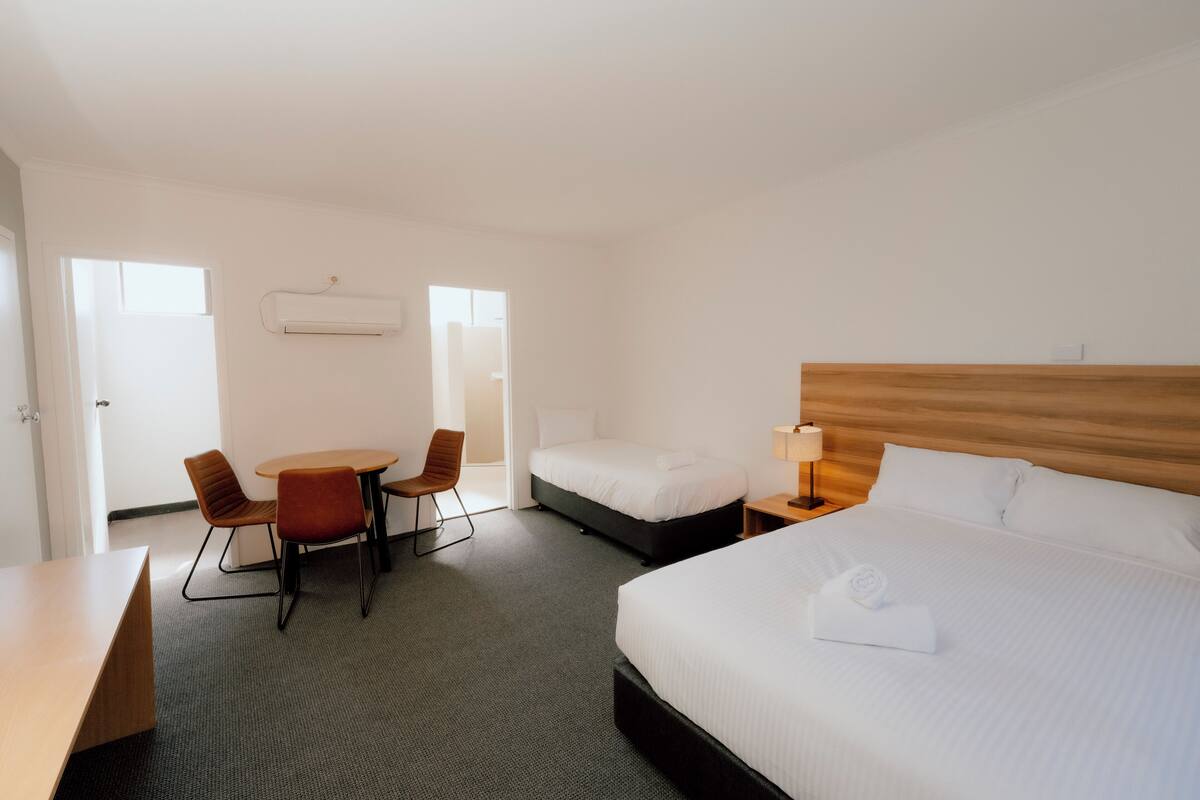 Une chambre d’hôtel comprenant un lit, un bureau, deux chaises, une petite table et une table de chevet avec une lampe.