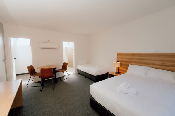 A hotel room with a bed, a desk, two chairs, a small table, and a nightstand with a lamp.
