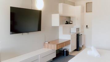 A hotel room with a bed, a desk with a computer, a TV, a microwave, and a trash bin.