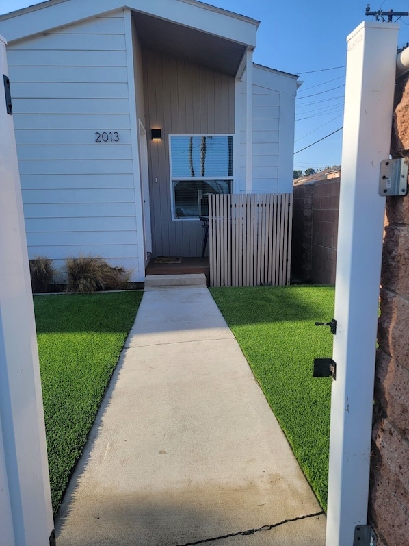 A pathway leading to a building with a number '2013' on the wall, a wooden fence, and a grassy area.