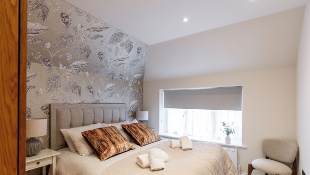 A bedroom with a bed, pillows, a chair, a nightstand, a lamp, and a window with a view. - New Apartment in Guildford (Guildford)