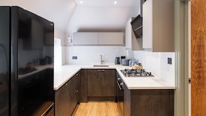 A modern kitchen with dark cabinetry, a white countertop, a built-in stove, and a black refrigerator. - New Apartment in Guildford (Guildford)