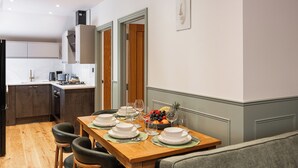 A dining area with a wooden table set for six, a fruit bowl, and a grey sofa in the foreground. - New Apartment in Guildford (Guildford)