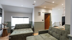 A modern living room with a sectional sofa, a small side table, and a window with curtains. - New Apartment in Guildford (Guildford)