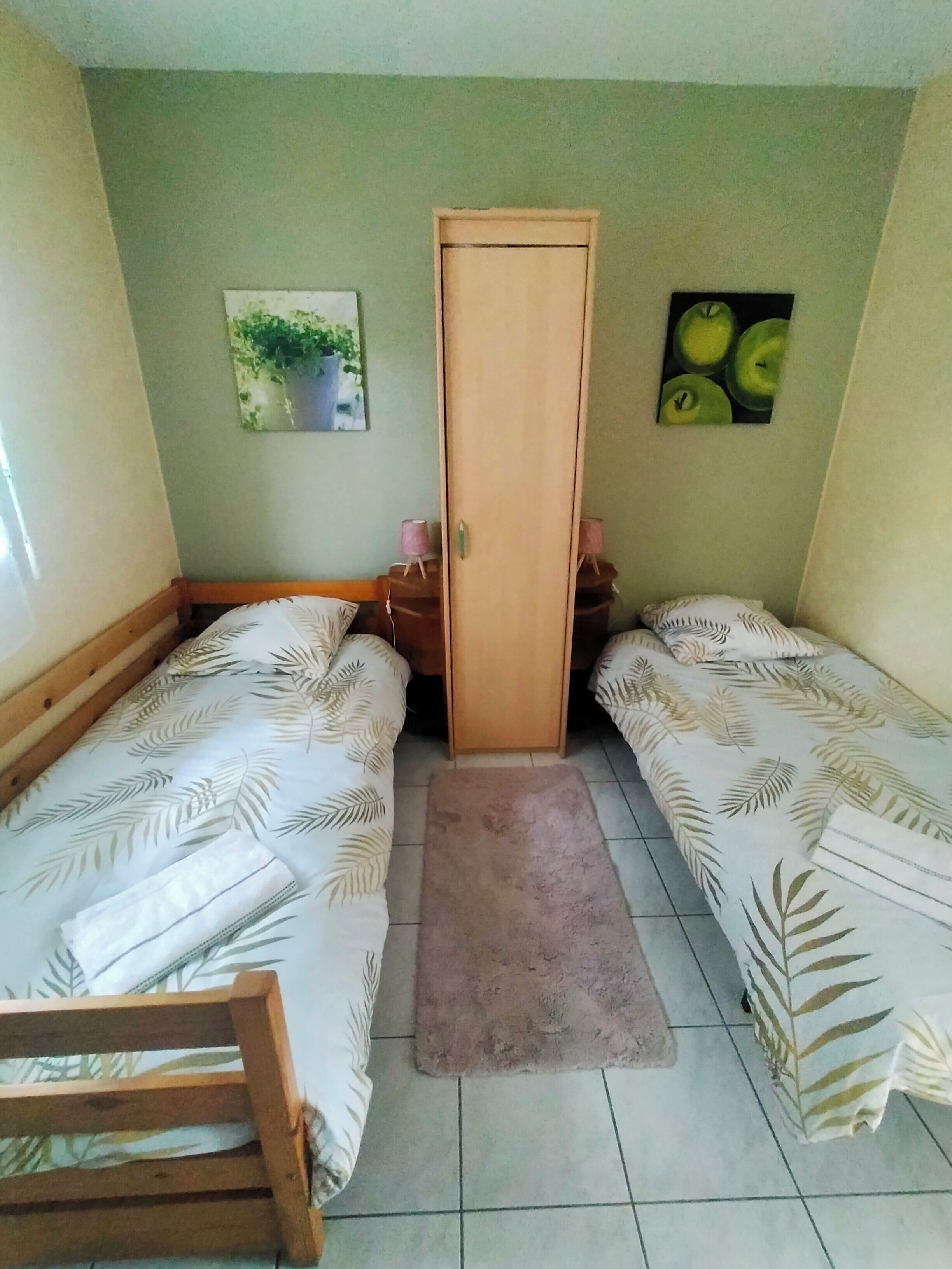 Une petite pièce avec deux lits, une armoire en bois, un petit tapis et deux lampes fixées au mur.