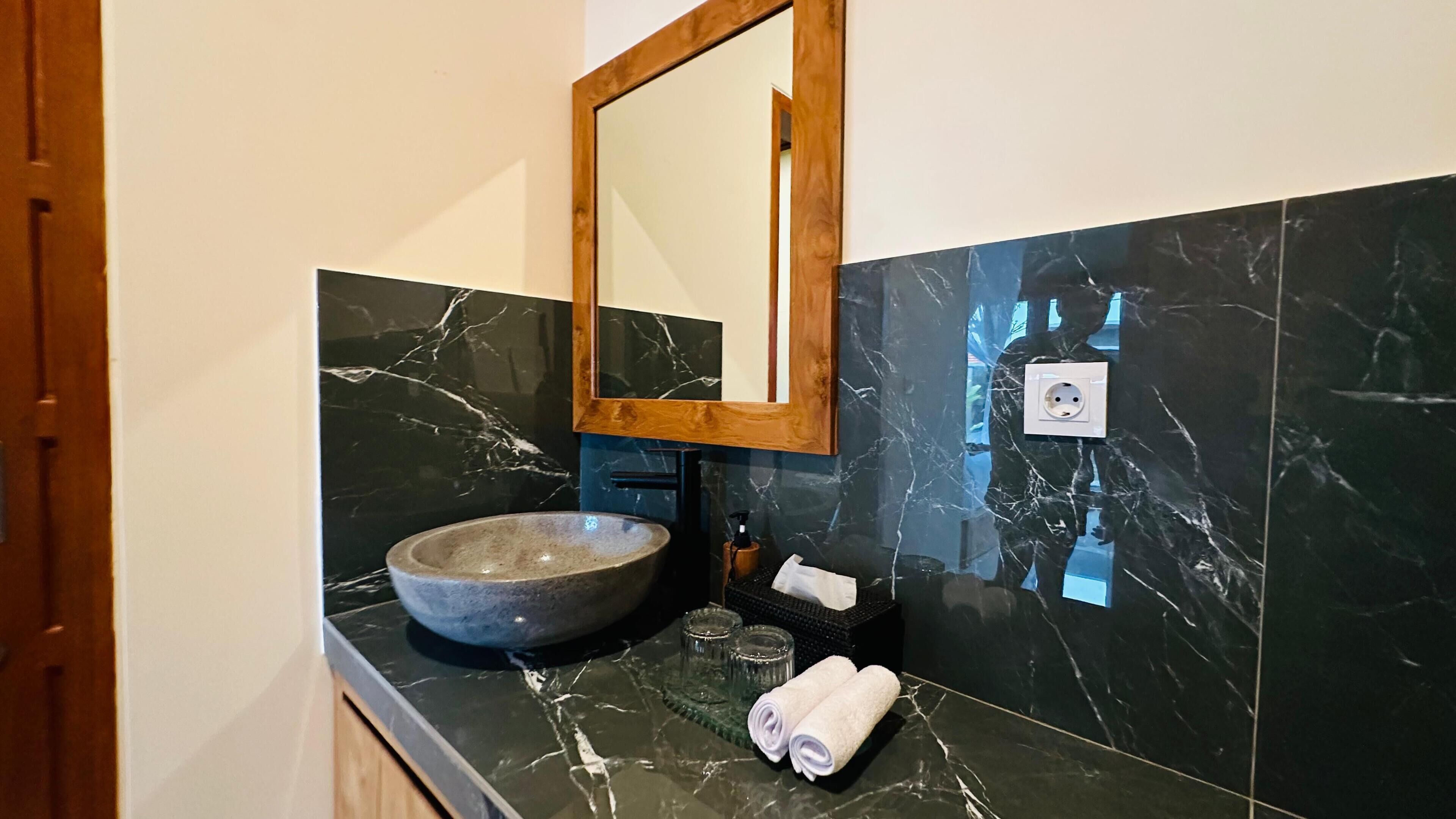 A bathroom with a large basin, a wooden-framed mirror, a towel, and a soap dispenser.