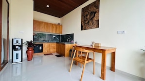 A modern kitchen with wooden cabinets, a marble countertop, a dining table with chairs, and a wall-mounted artwork. - Villa Uma Asri (Ubud)