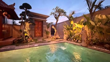 Una piscina con borde de piedra, rodeada de plantas tropicales y una estructura de madera.