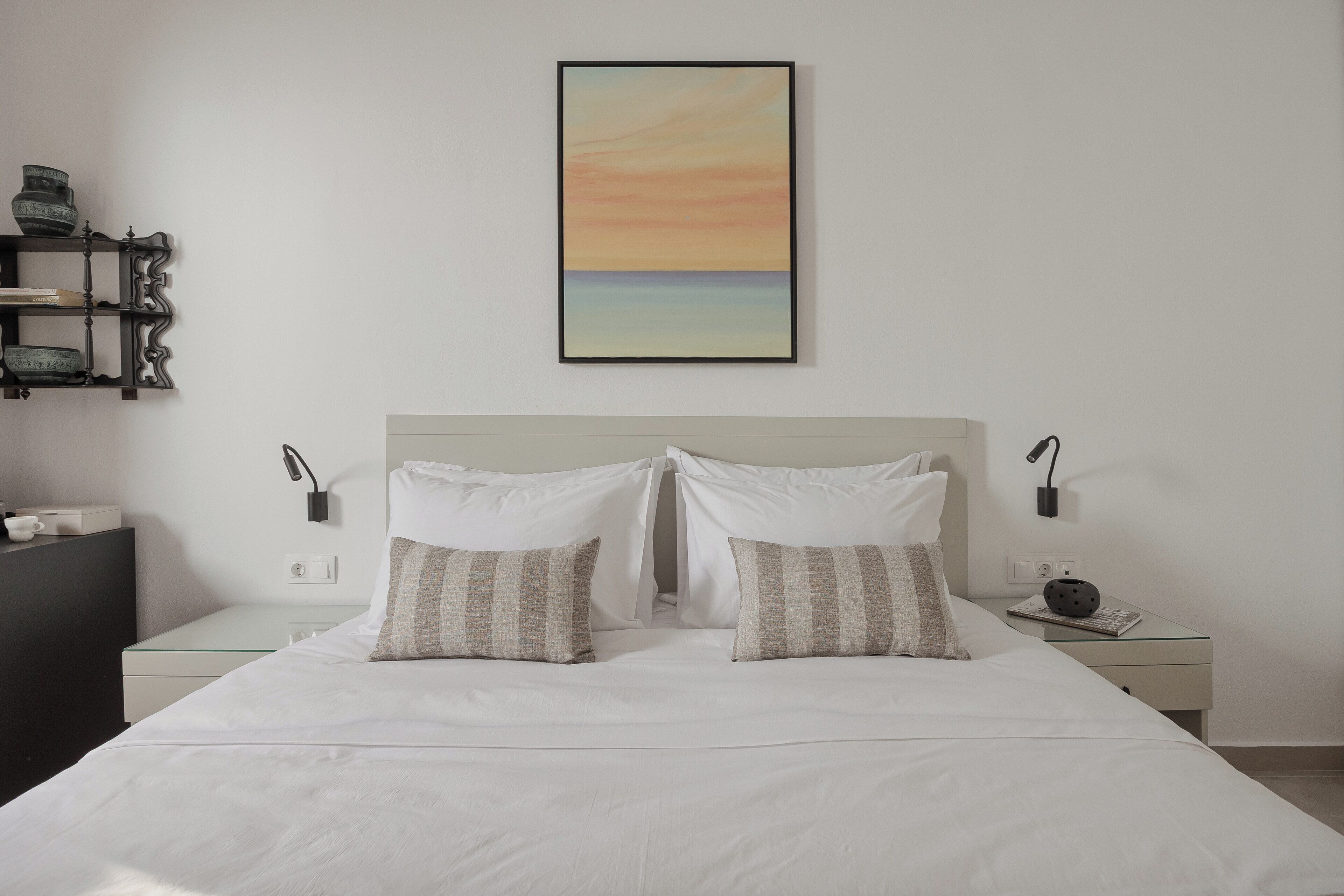 A neatly made bed with two pillows, a bedside table with a lamp, and a wall-mounted picture.