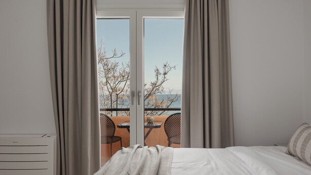 A bedroom with a bed, a radiator, and a view of an outdoor terrace with chairs and a table.
