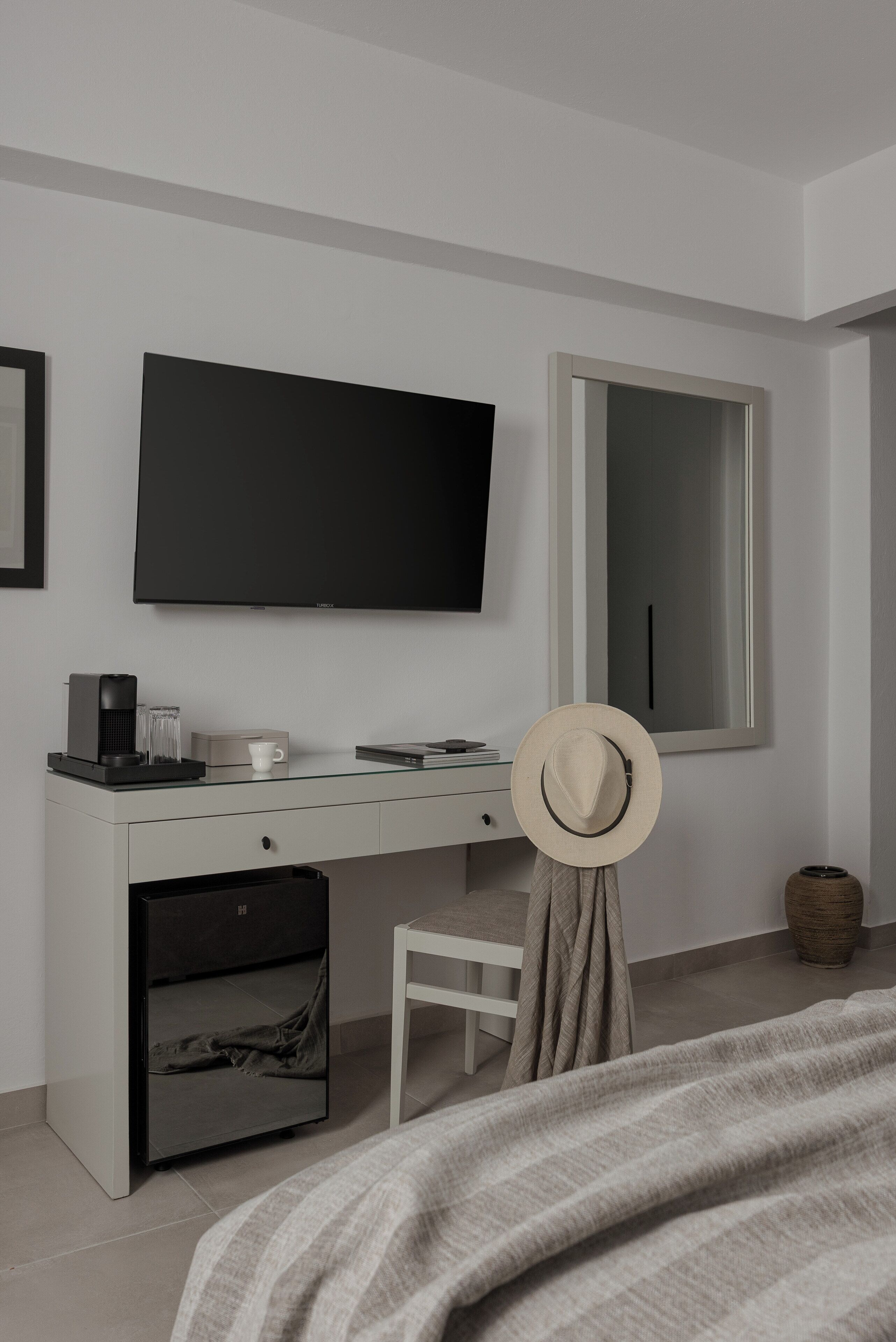 A modern bedroom with a bed, a TV, a desk with a computer, and a mirror.