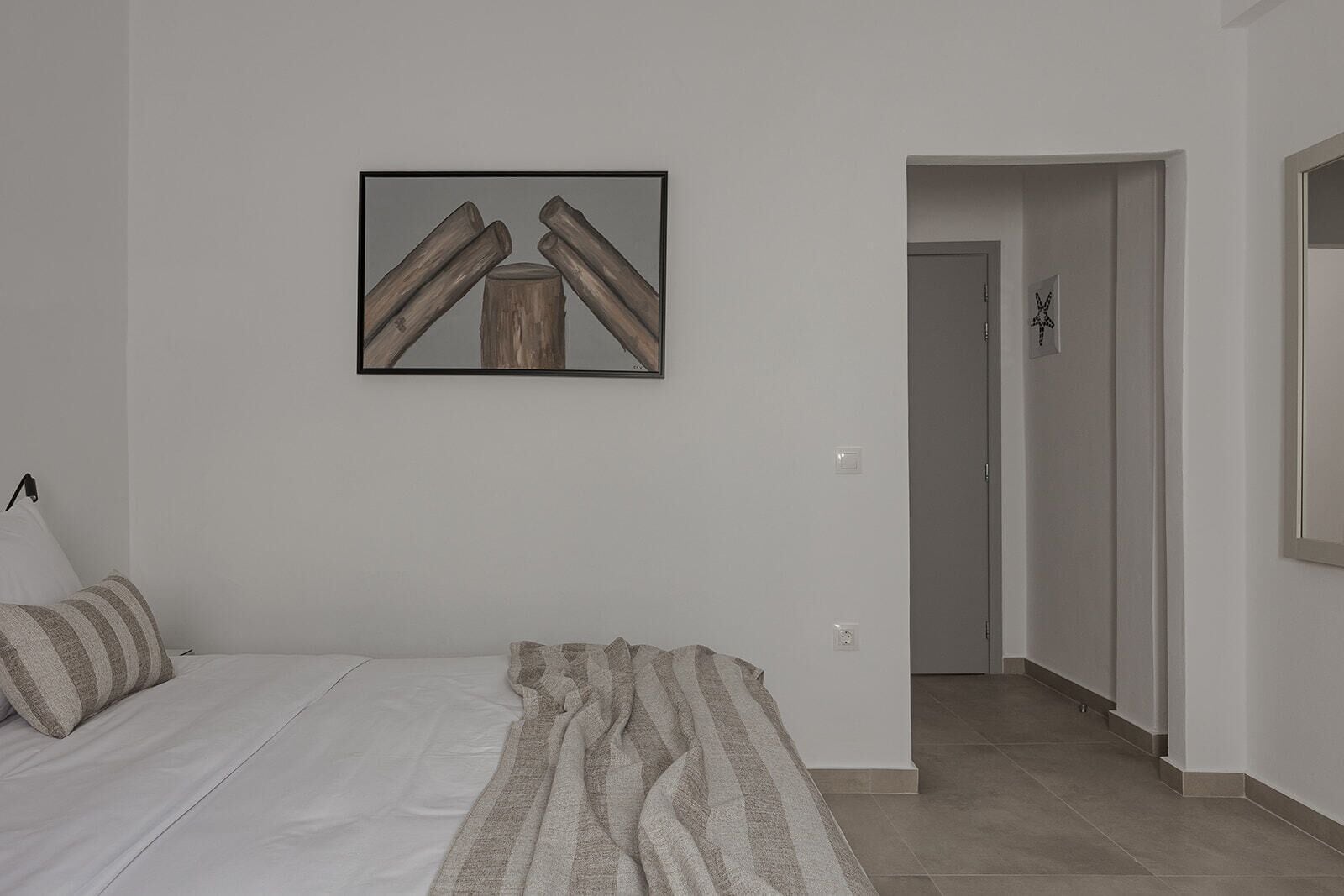A bedroom with a bed, pillows, a blanket, a framed picture on the wall, and a hallway leading to another room.