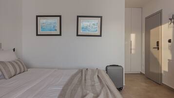 Ein Hotelzimmer mit einem Bett, einem Koffer, zwei gerahmten Bildern an der Wand und einer Tür.