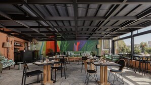 An indoor dining area with tables and chairs, a bar area, and a colorful mural on the wall.