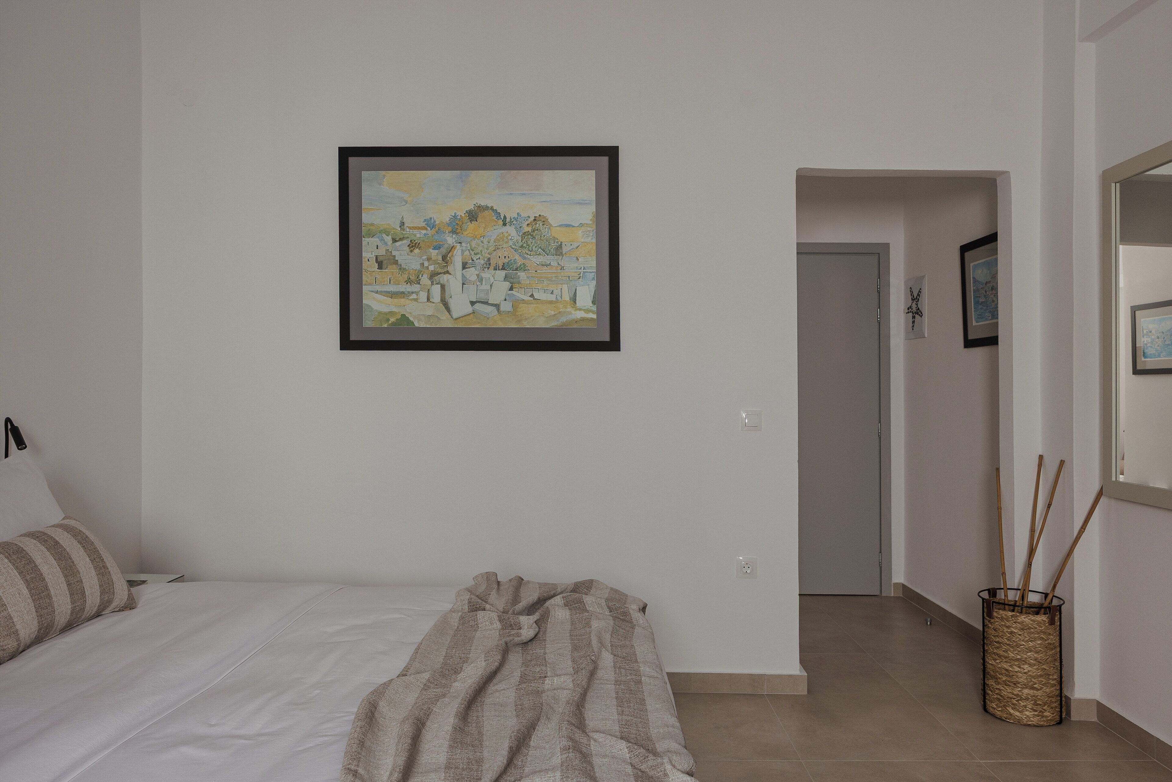 Une chambre à coucher avec un lit, une couverture, un tableau encadré accroché au mur et un couloir menant à une autre pièce.