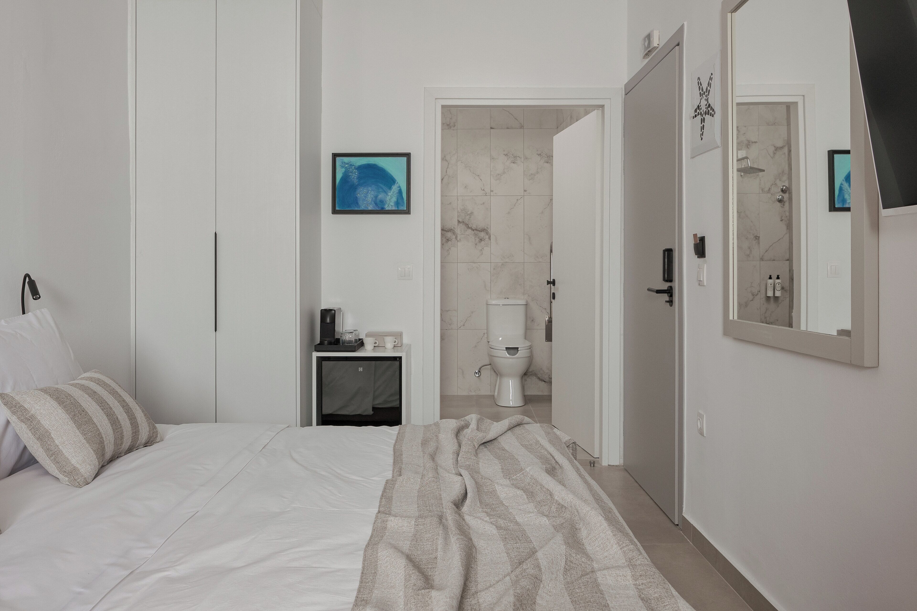 A bedroom with a bed, a bedside table with a lamp, a bathroom with a toilet and shower, and a mirror on the wall.