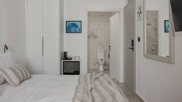 A bedroom with a bed, a bedside table with a lamp, a bathroom with a toilet and shower, and a mirror on the wall.