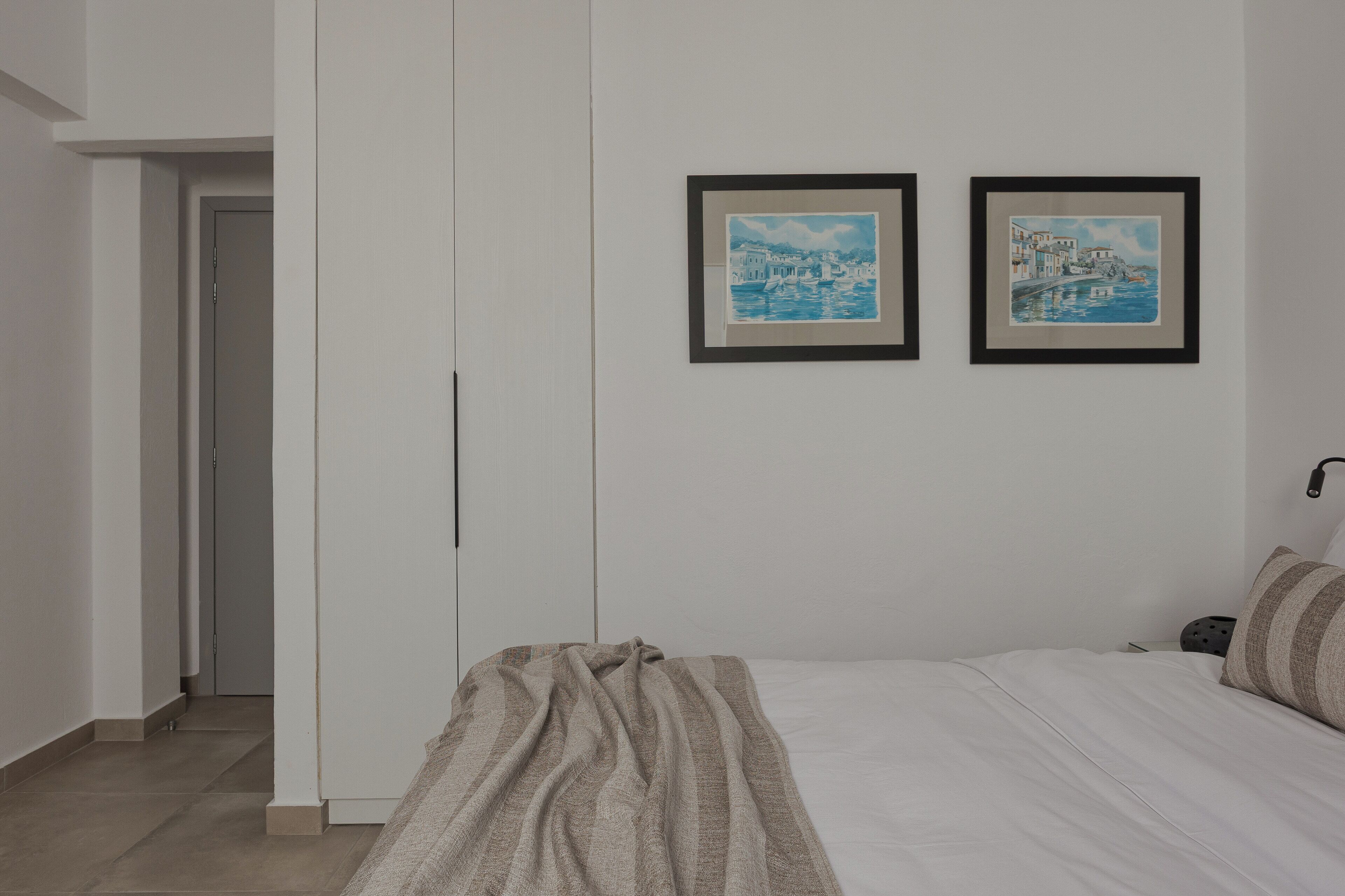 A bedroom with a bed, a wardrobe, and two framed pictures on the wall.