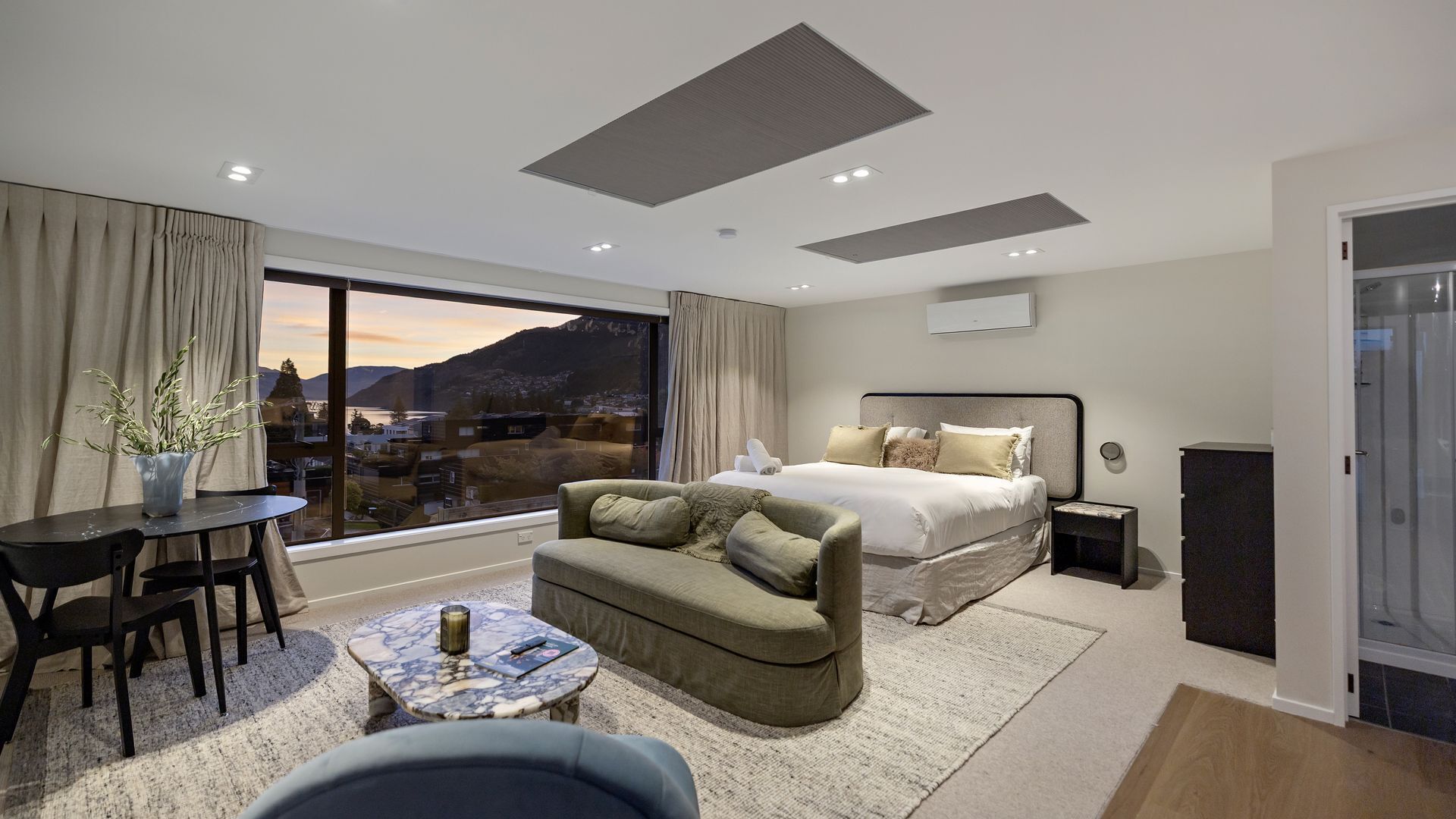 Une chambre d’hôtel moderne dotée d’un grand lit, d’un canapé, d’un coin repas et offrant une vue sur le paysage urbain.