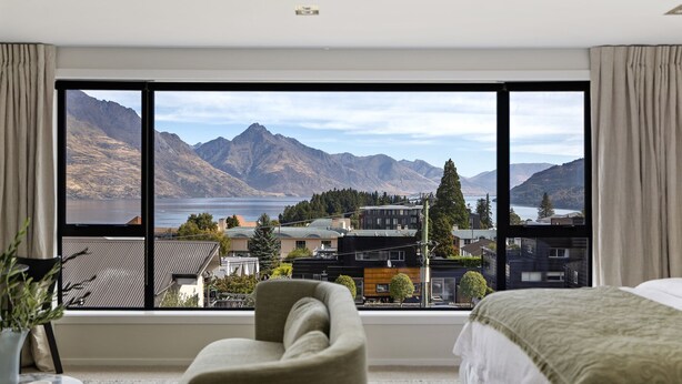 A bedroom with a large window offering a view of mountains and a lake. - Queenstown Hill House - Studio Only. Lakeview Room, with a prime location and kitchen. (Queenstown)