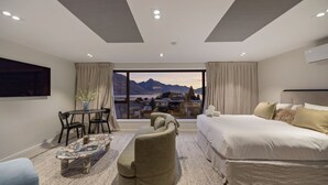 A modern hotel room with a large bed, a seating area with a table, and a view of mountains through the window. - Queenstown Hill House - Studio Only. Lakeview Room, with a prime location and kitchen. (Queenstown)