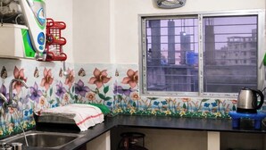 A kitchen with a gas cylinder, a kettle, and a window with a view of buildings. - Arjun Guest House (Bidhannagar)