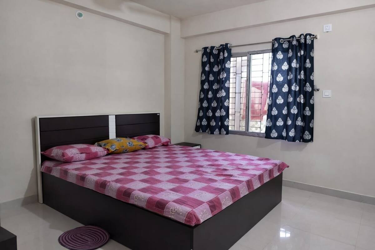 A bedroom with a bed, a window with patterned curtains, and a tiled floor.