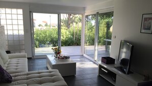 A modern living room with a sofa, coffee table, TV, and sliding glass doors leading to a patio. - AGATHOISE MAS at CAP D'AGDE (Agde)