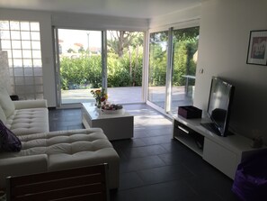 Ein modernes Wohnzimmer mit einer Couch, einem Couchtisch, einem Fernseher und einer Glasschiebetür, die auf eine Terrasse führt.