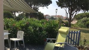 An outdoor patio with a table and two chairs, surrounded by lush greenery and a view of buildings in the distance. - AGATHOISE MAS at CAP D'AGDE (Agde)