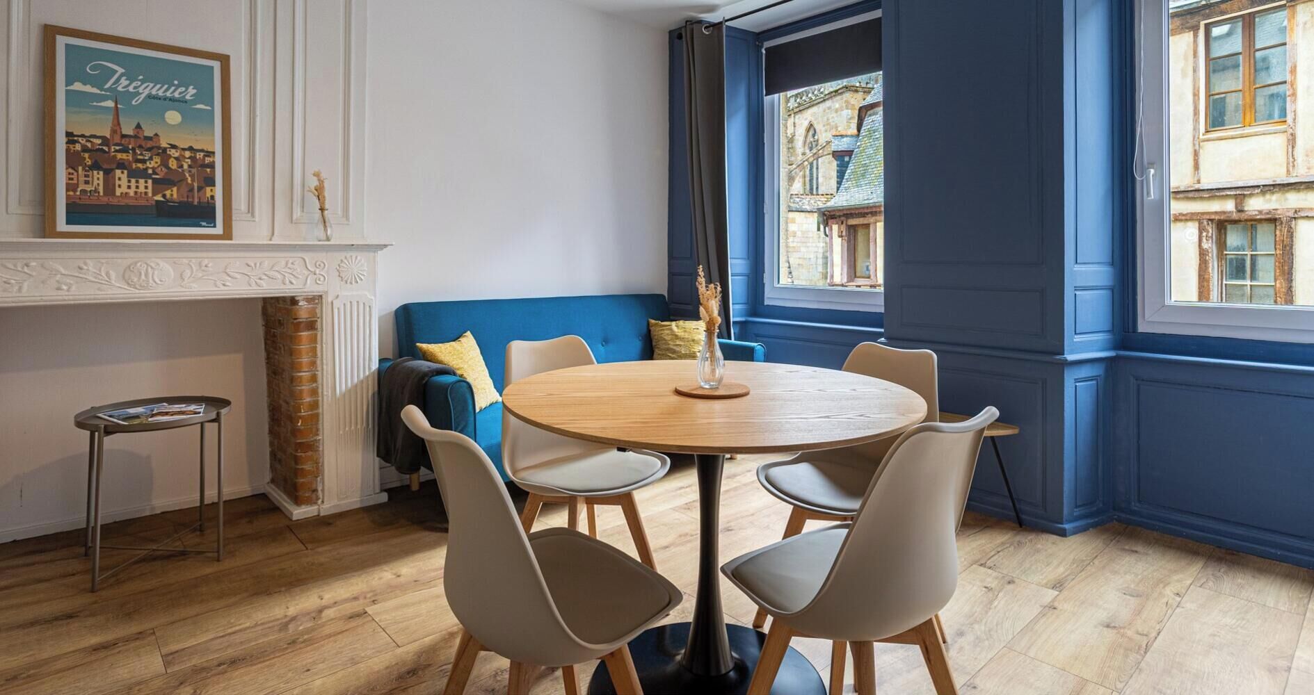 A dining area with a round table, chairs, a blue sofa, a small side table, and a fireplace.