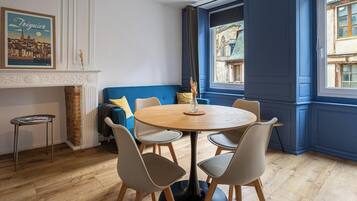 A dining area with a round table, chairs, a blue sofa, a small side table, and a fireplace.
