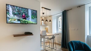 En moderne stue med et fladskærms-tv, et spiseområde med et bord og stole, samt en teal farvet lænestol.