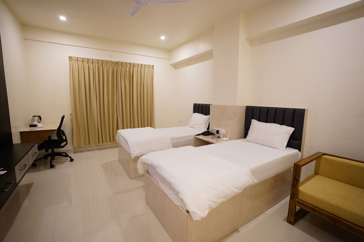 A hotel room with two beds, a desk with a chair, a TV, and a window with curtains.