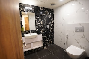 A modern bathroom with a white sink, black marble walls, a white toilet, and a mirror.
