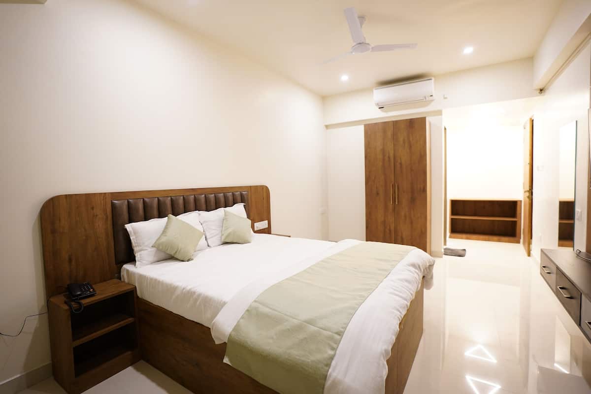 A bedroom with a wooden headboard, a bed with white bedding, a nightstand with a phone, a ceiling fan, and an air conditioning unit.